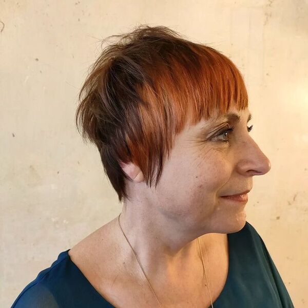 Pixie Cut with Copper Hair Bangs: una mujer con una blusa azul oscuro y un collar