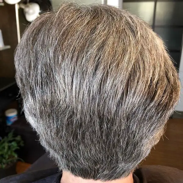 Corte de pelo Pixie corto: una anciana en un salón con una capa negra