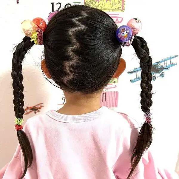 Zigzag Dos peinados de cola de caballo trenzados para niñas: una niña con suéter rosa.