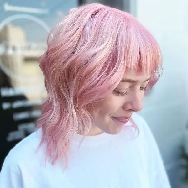 una mujer con una camisa blanca tiene un cabello corto de color rosa pastel