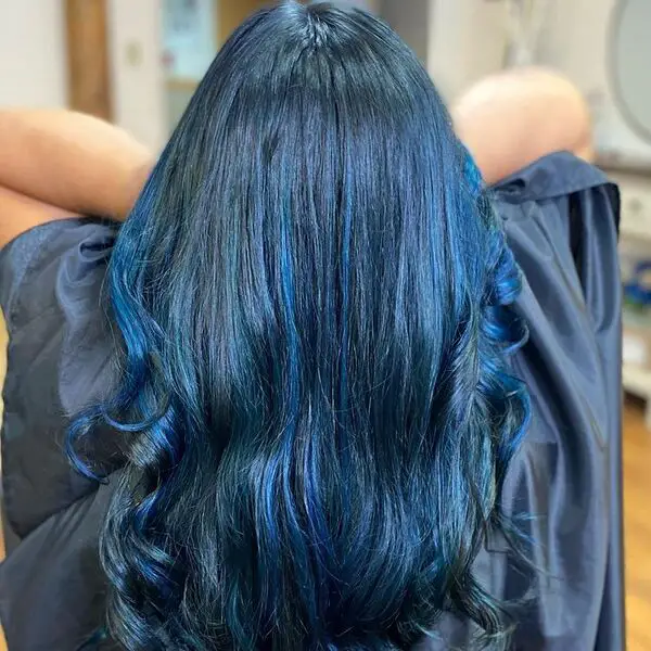 Cabello azul negro brillante: una mujer que sostiene su cabello lleva una capa de salón