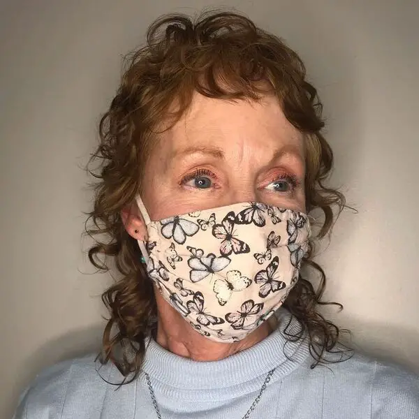 Curl Mullet en Mujeres mayores de 50 años: una mujer con una máscara de mariposas y un top azul pastel.