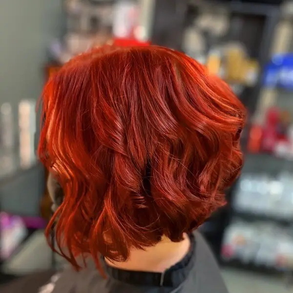 Curly Chili Red Hair Color: una mujer en un salón con una capa negra