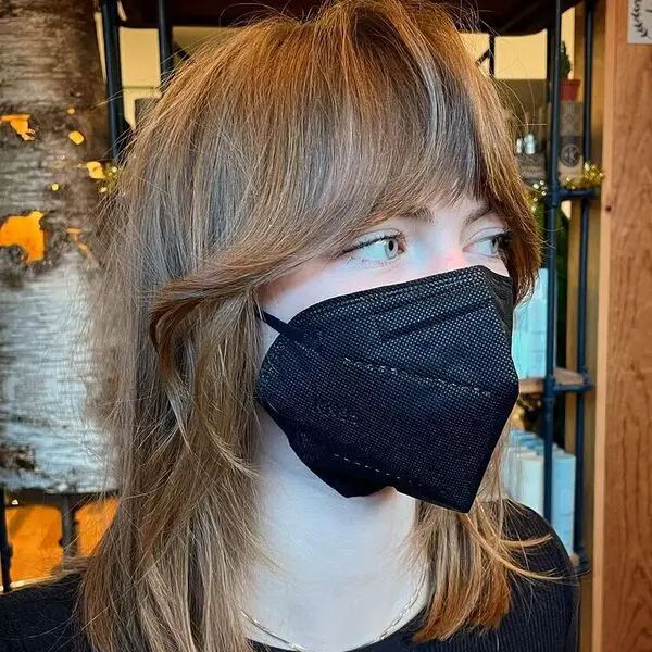 Corte romo de inspiración parisina con flequillo de cortina: una mujer con una máscara negra y una camisa negra